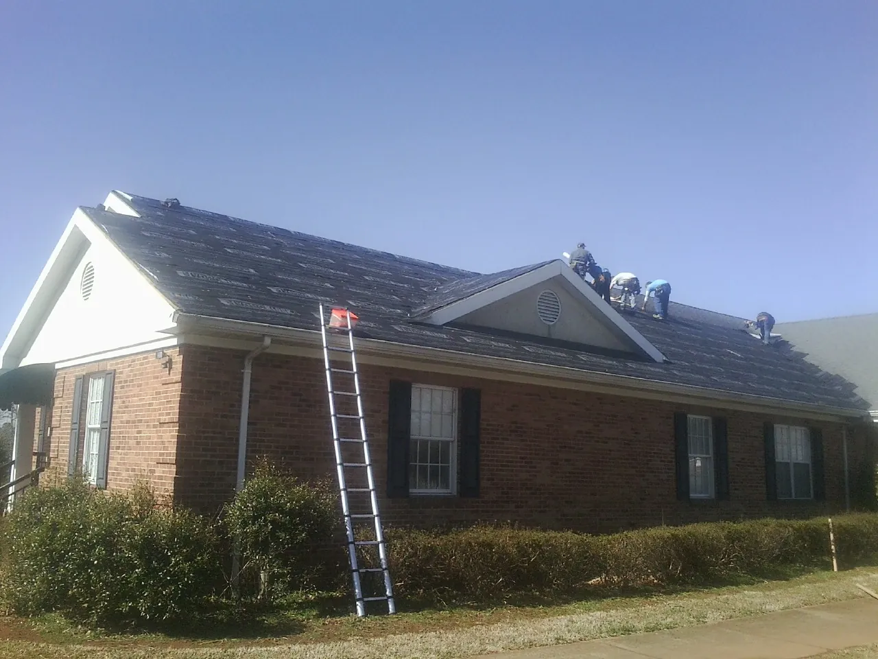Crew tearing shingles off a brick ranch roof with a ladder set — Emergency Roof Repair work by our crew in Portage