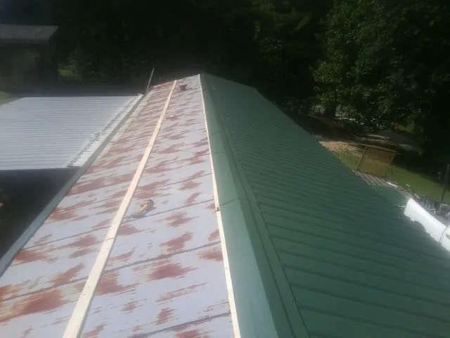 Old rusted panels beside newly installed green metal roofing — Wind Damage Roof Repair by Roofing Brothers in Portage