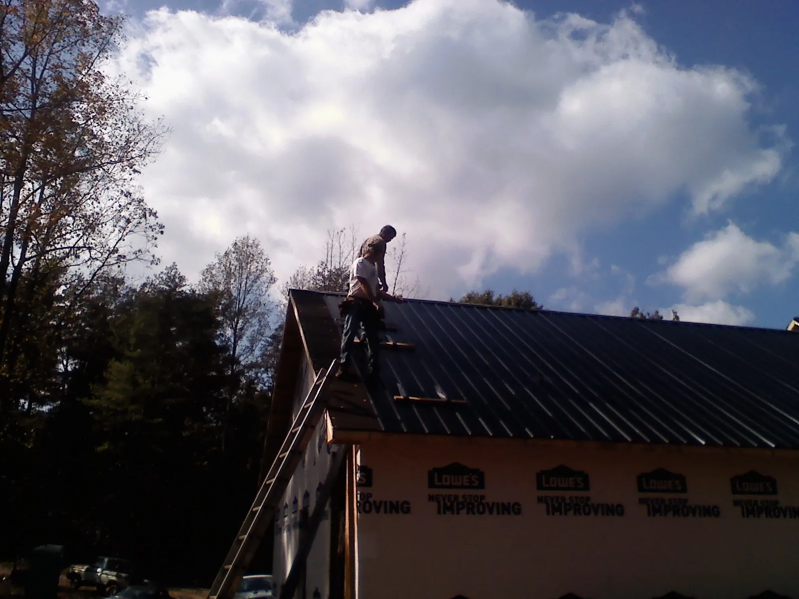 Roofer fastening dark metal panels high against a cloudy sky, from a Roof Inspection job in Portage